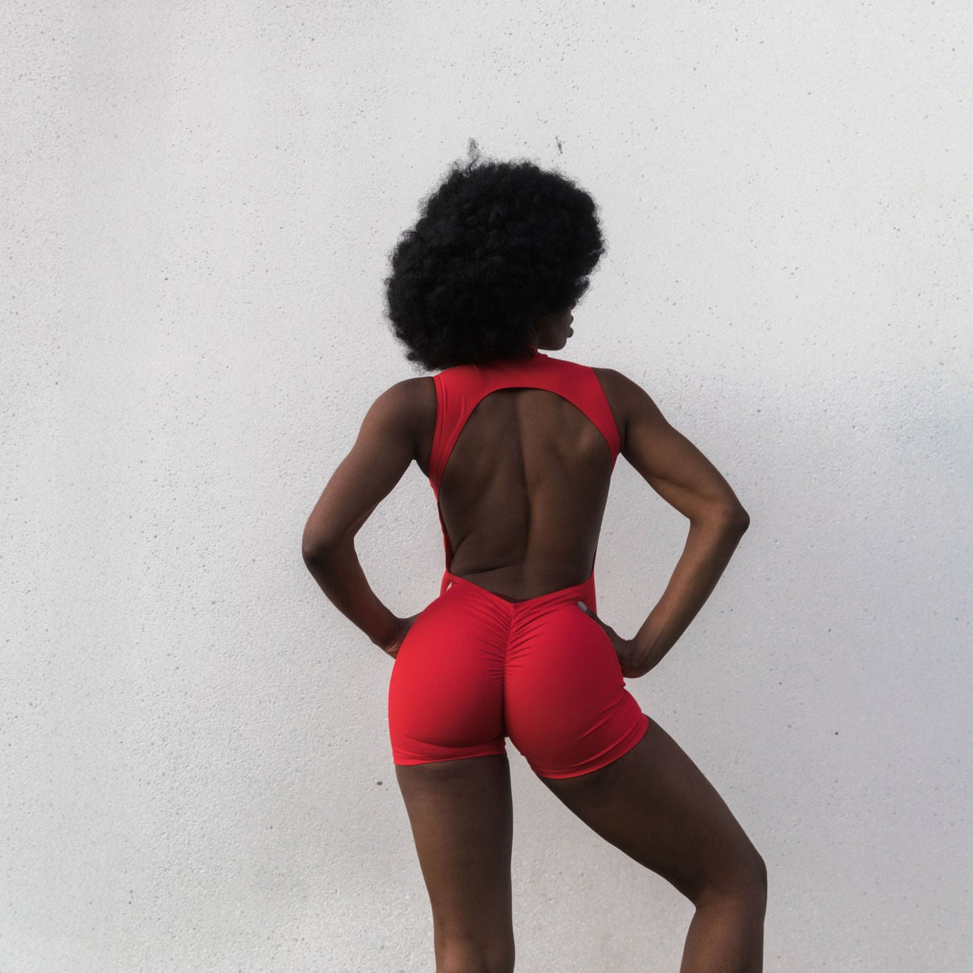 Model with afro hairstyle in red sculpt romper, back view — The Palm activewear