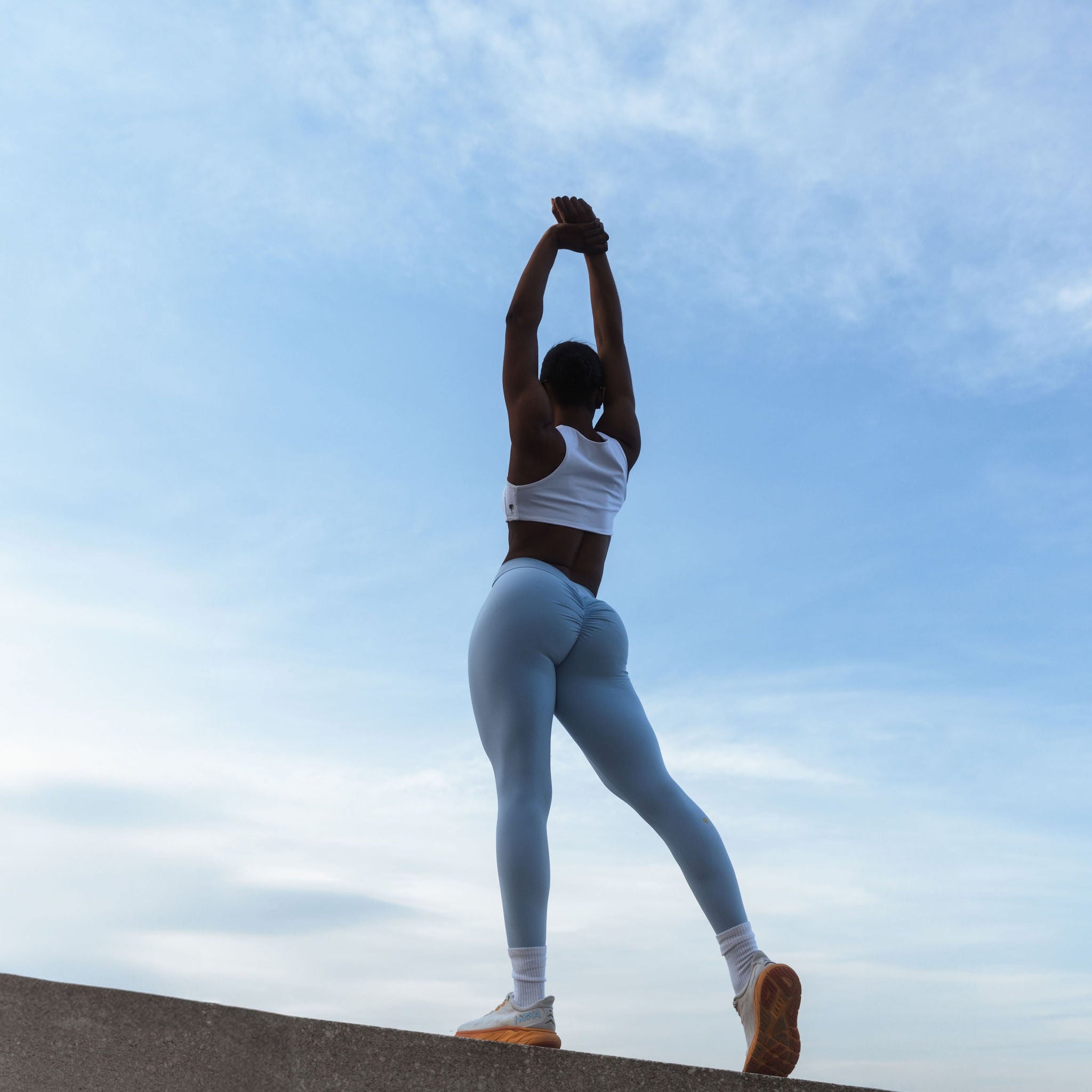 Activewear set by The Palm. White seamless bra and sky blue leggings, stretching under morning sky.