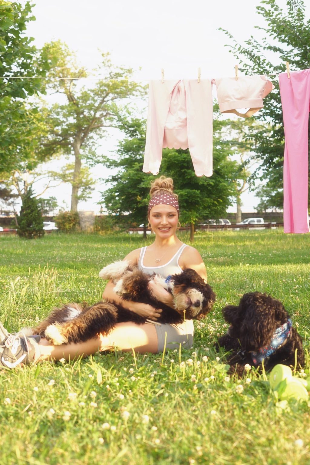 Woman in The Palm activewear sitting on grass with two dogs beneath a clothesline of activewear
