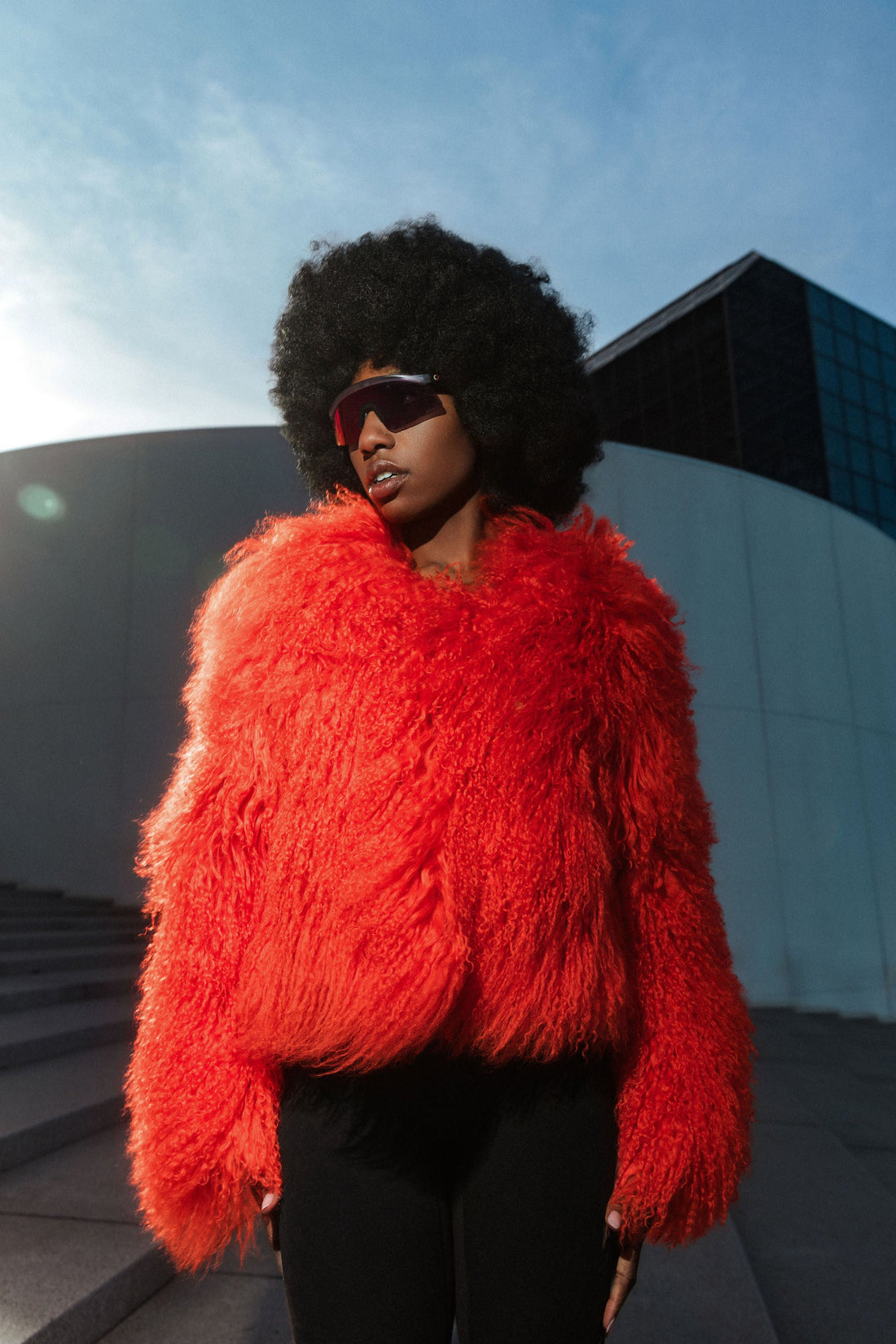 Fashion-forward New York portrait in a vivid red statement coat and visor sunglasses
