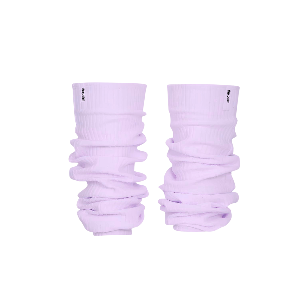 Ivory ribbed knit leg warmers by The Palm, featuring a minimalist logo tag and soft slouchy texture on a lilac mist background1