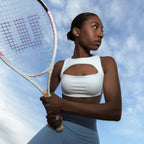 Model in The Palm activewear set with tennis racket and sky background. Clean aesthetic.