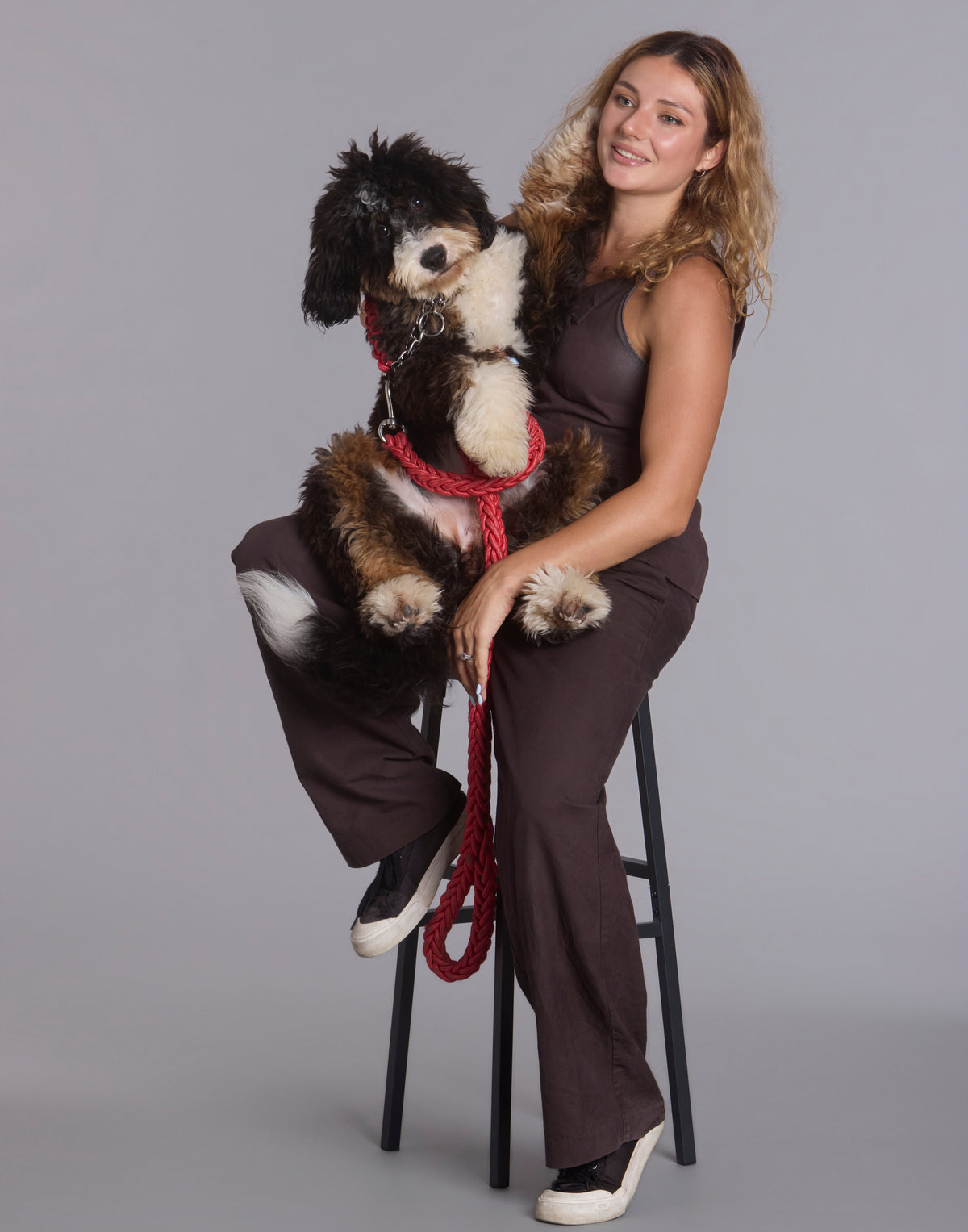 Smiling woman seated on a bar stool holding a fluffy dog with a red braided leash The Palm