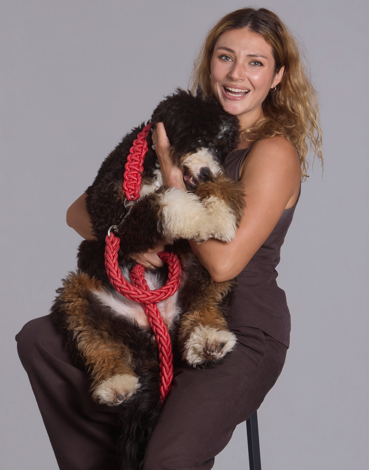 Close-up studio portrait of smiling woman holding her fluffy dog on a red braided leash The Palm