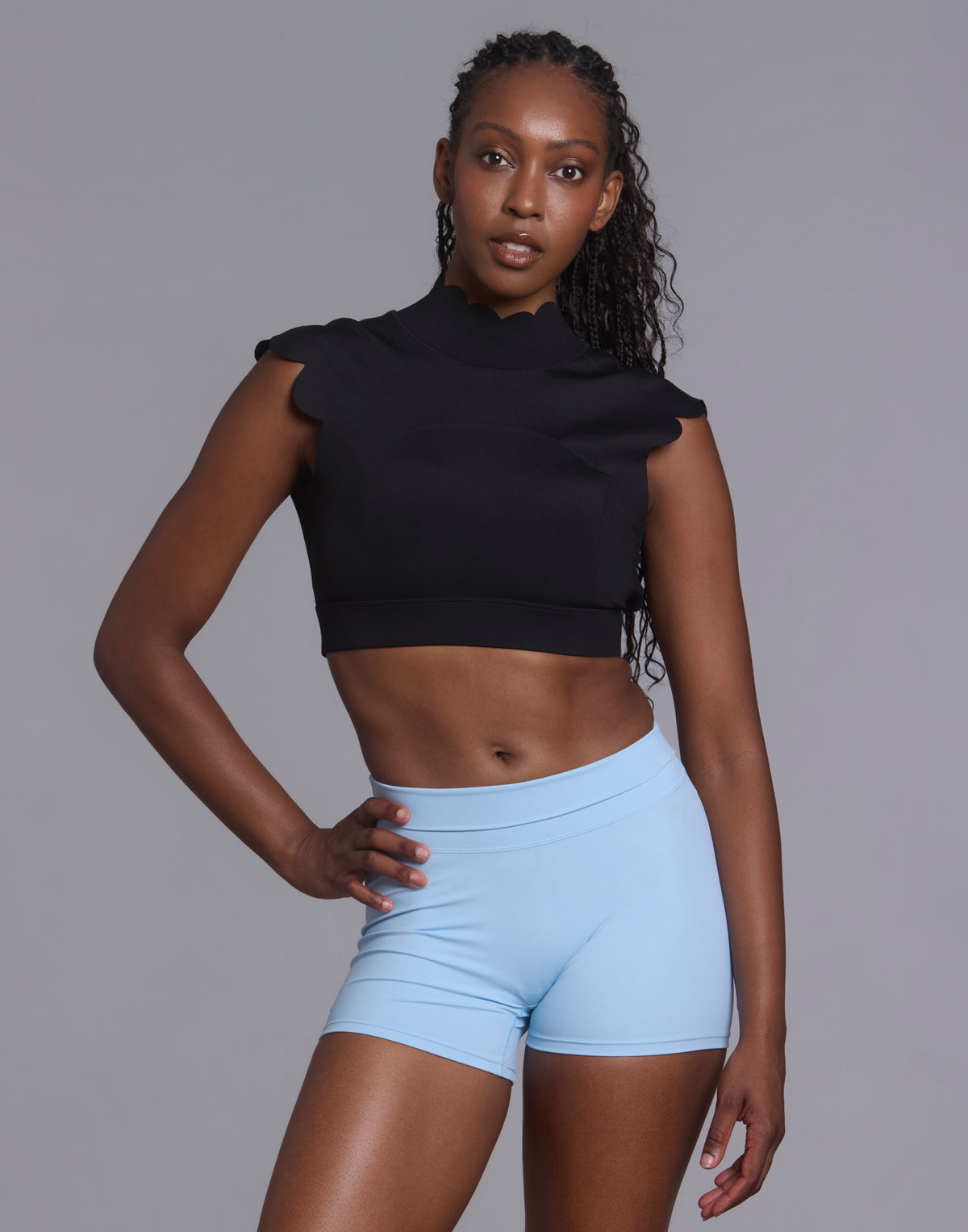 Front studio view of athletic woman wearing black CloudPetal mock-neck cropped top and light blue shorts