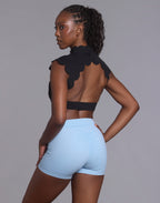 Back studio view of woman wearing black CloudPetal top showing open back design with light blue shorts
