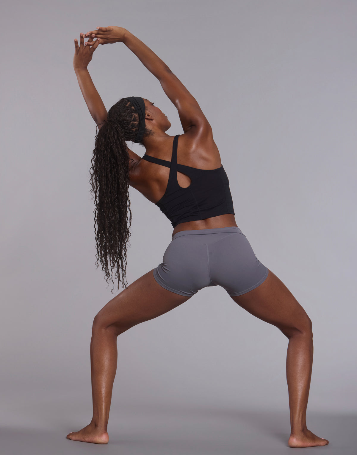 Back view of athletic woman in wide stretch pose wearing black CrossForm sculpt tank top and grey shorts