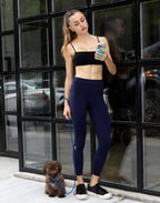 Front full-length view of woman holding smartphone standing with dog wearing high-waisted dark blue LiftLine sculpt leggings