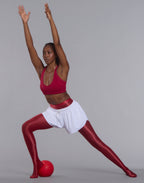 Dynamic studio shot of athletic woman stretching with arms overhead wearing red PalmLift bra and white shorts
