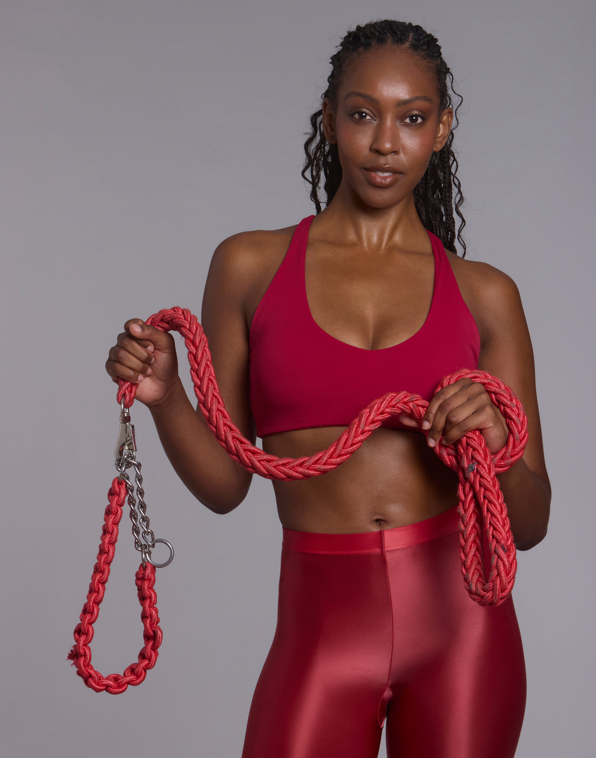 Front-facing studio shot of athletic woman holding red braided rope wearing red PalmLift sports bra and shiny red leggings
