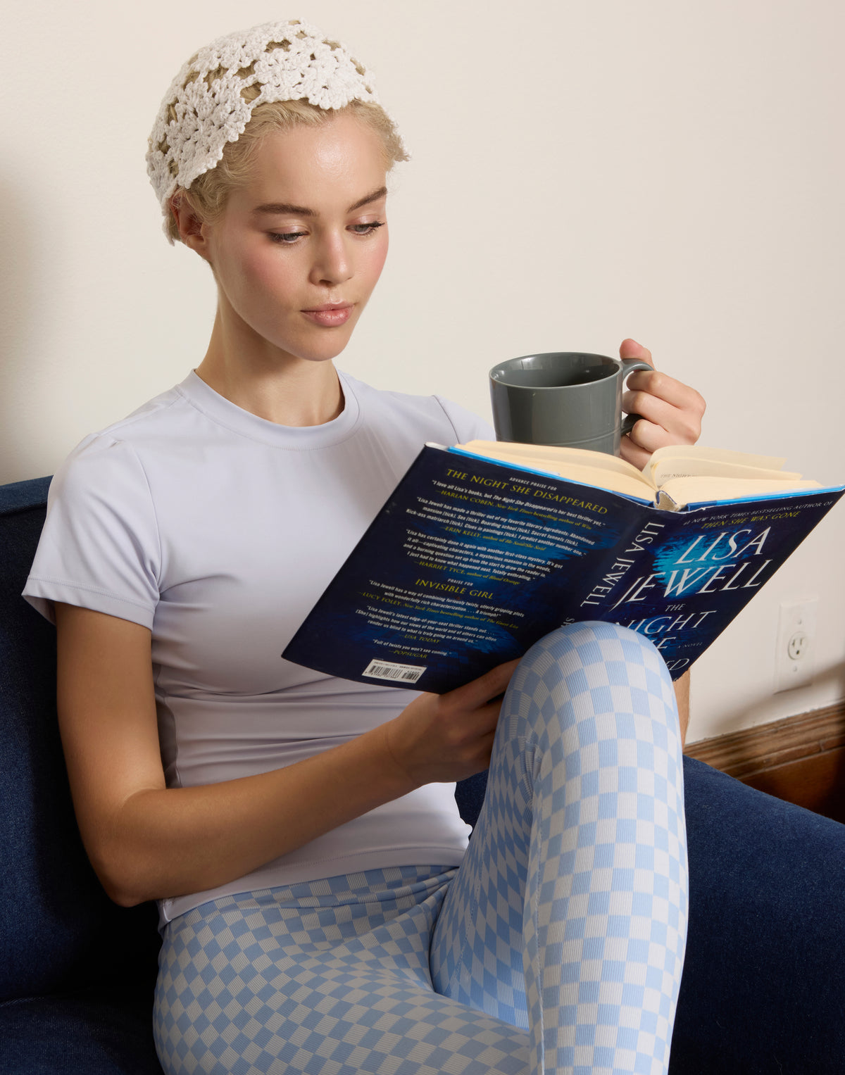 Woman relaxing on couch reading a book wearing QuadFit light blue checkerboard high-waisted leggings