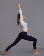 Woman in warrior yoga pose with arms overhead wearing white WrapLuxe cropped wrap top and dark leggings